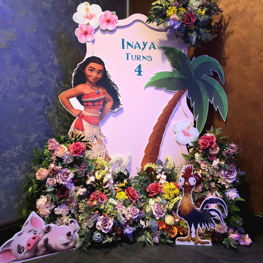 Moana-themed 4th birthday backdrop with floral arrangements, palm tree design, and character cut-outs of Moana, Pua, and Hei Hei.