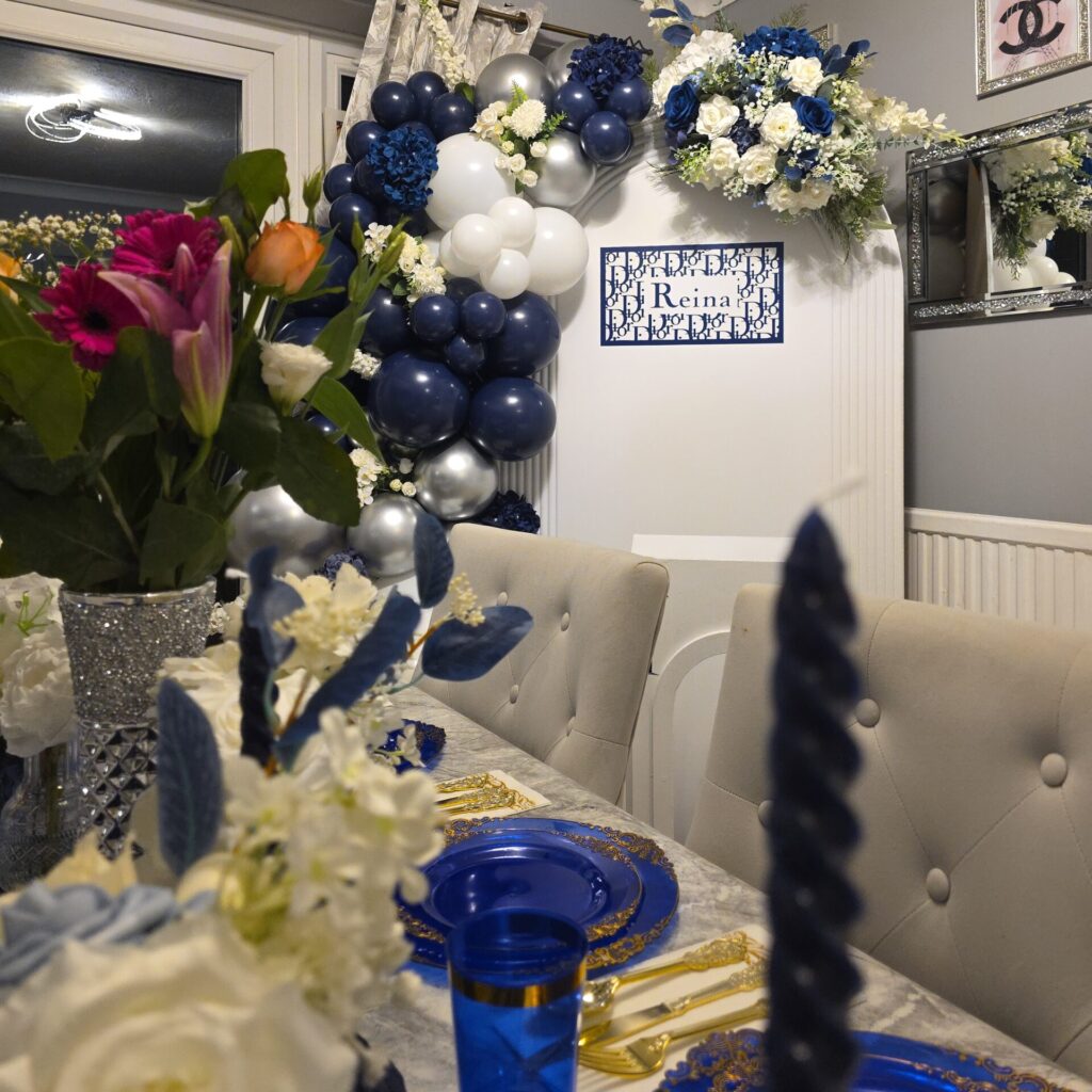 Dior-inspired private dinner setup with blue and white balloon garland, elegant floral arrangements, and a decorated dining table with blue and gold plates.