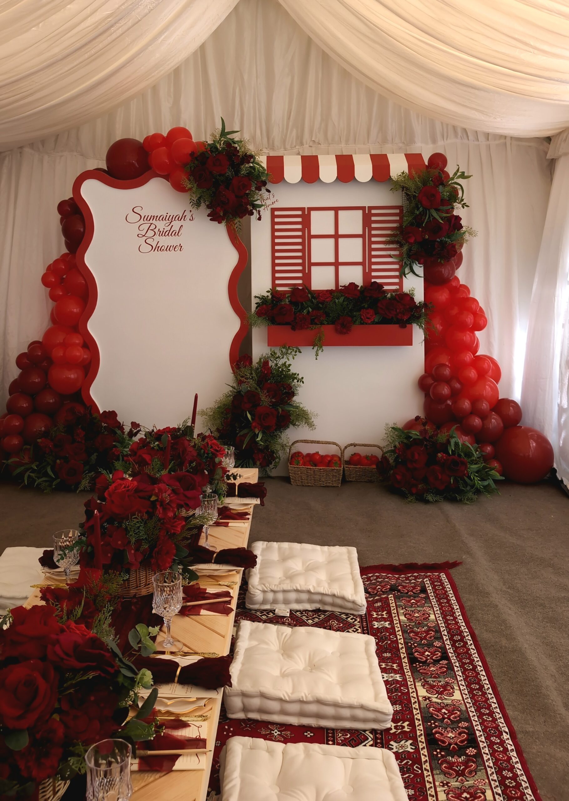 Intimate bridal shower table setup with floor cushions, floral centrepieces, and burgundy details.