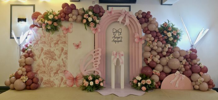 Blush and nude balloon arch with butterfly and bow themed personalised Aqiqah backdrop in East London