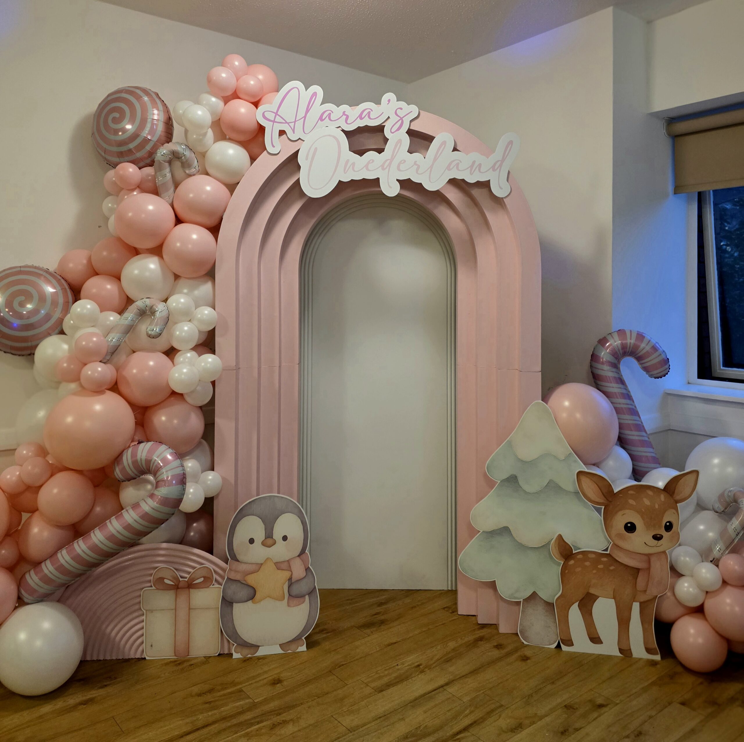 Large pastel arch backdrop with Winter Wonderland sign, penguin and deer props.