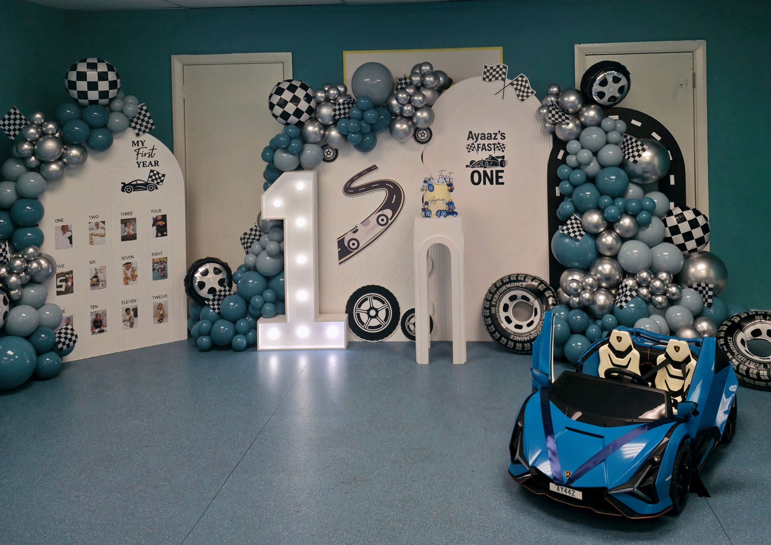 Full themed backdrop with racing panels, milestone board and a blue children’s toy car.