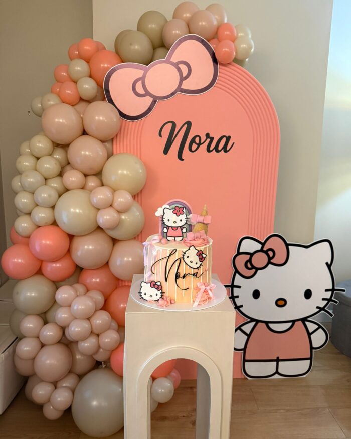Hello Kitty themed birthday backdrop with personalised arch panel and matching cake on a plinth.