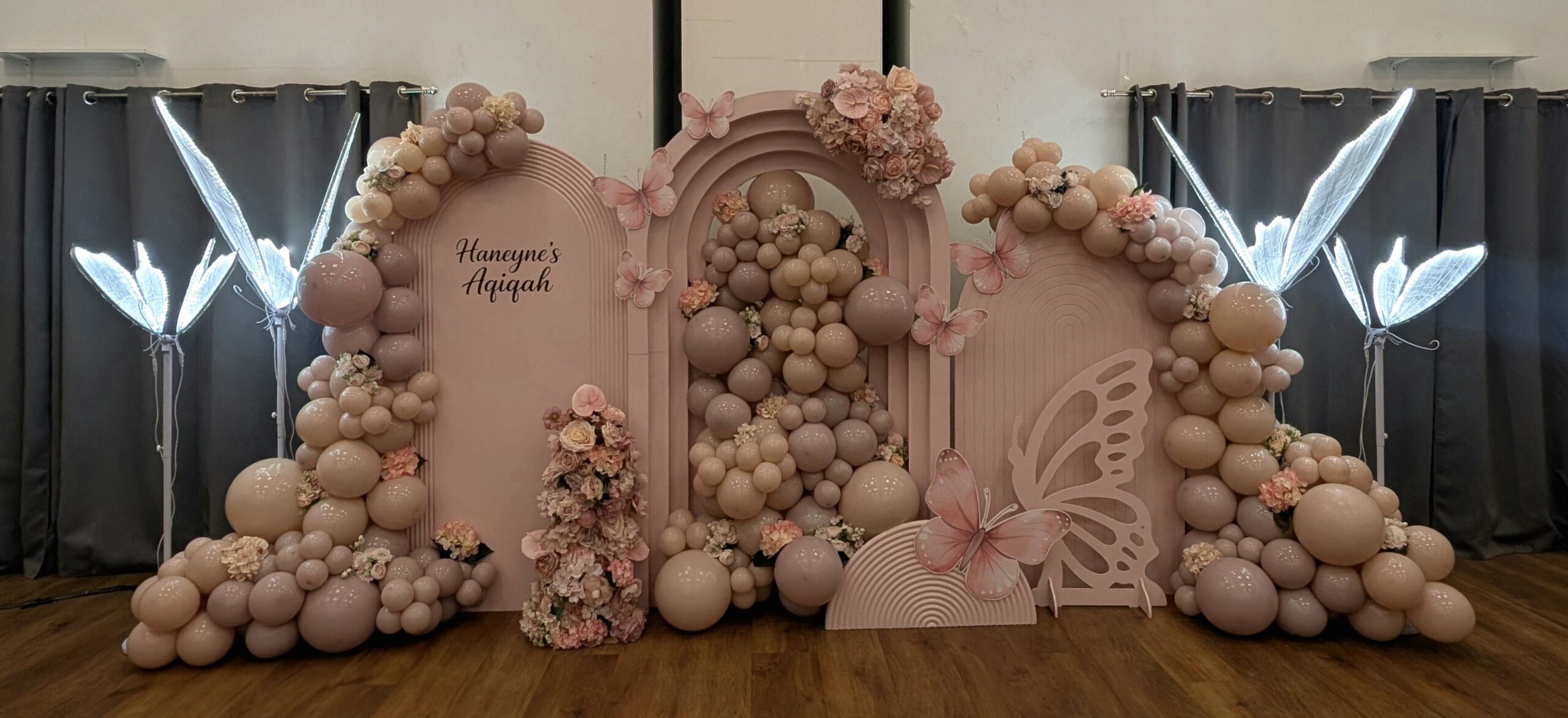 Blush and neutral butterfly-themed aqiqah backdrop with layered arches, balloons and florals for Haneyne’s aqiqah in Burnham.