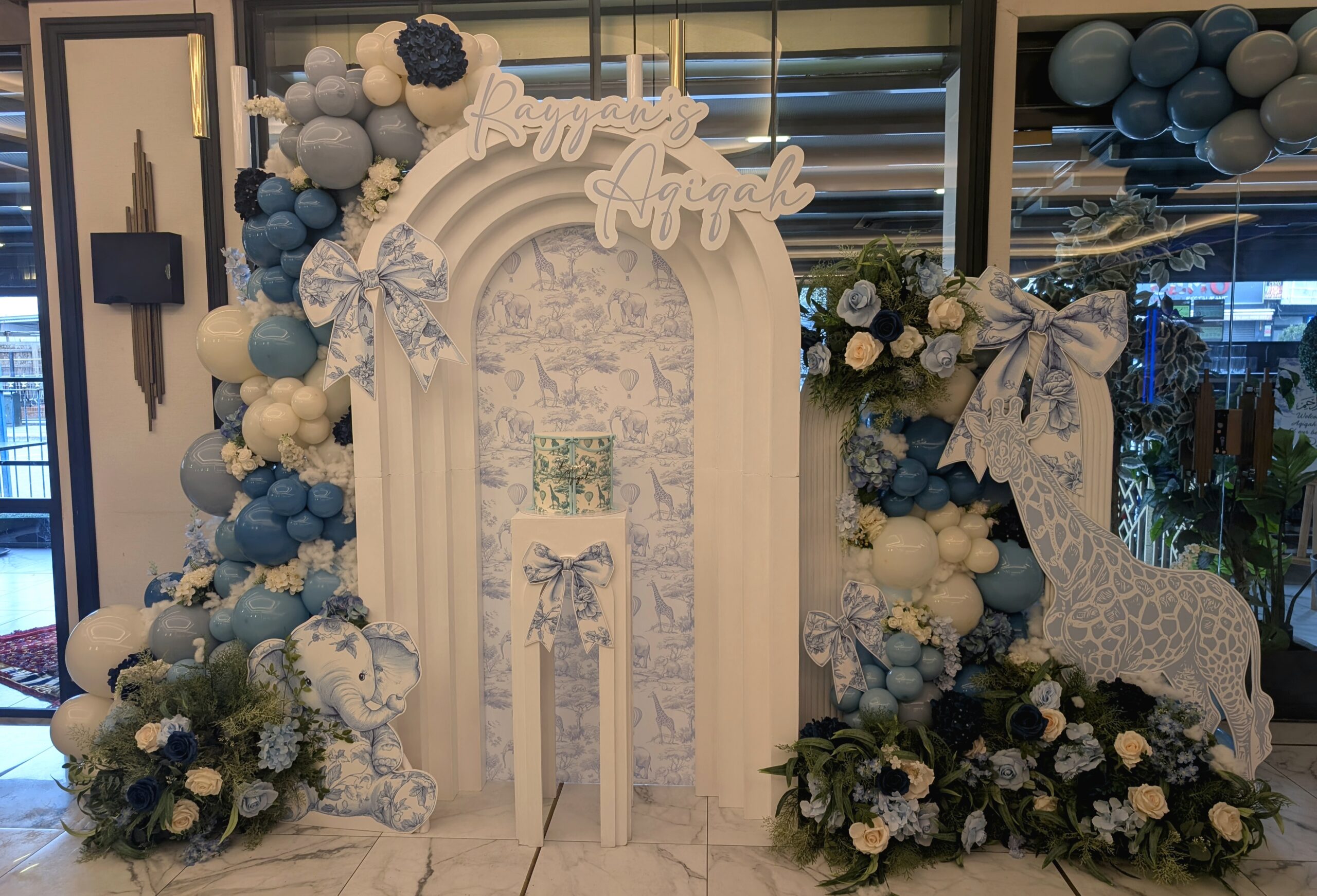 Blue and white safari themed aqiqah decor for Rayyan at Colony Restaurant featuring a personalised arched backdrop, balloon styling and floral arrangements.