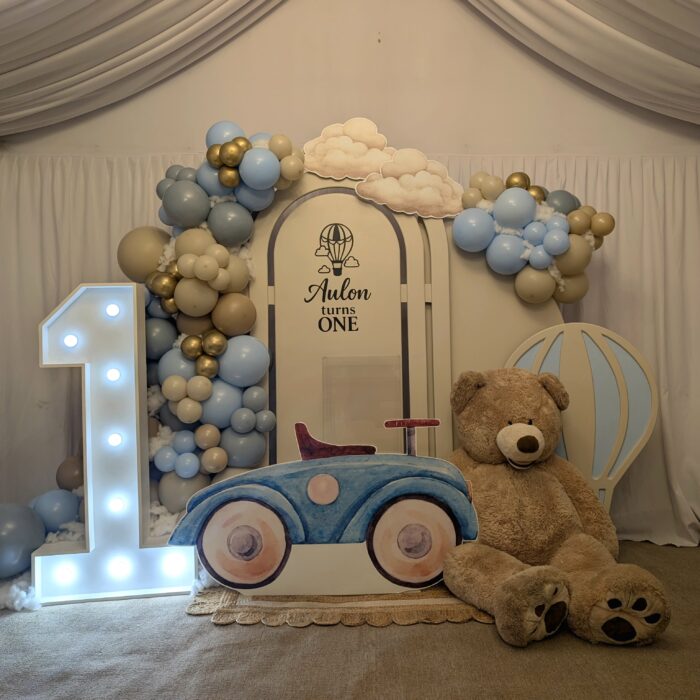 Teddy bear hot air balloon themed first birthday backdrop with personalised arch reading “Aulon Turns One”, balloon garland and light up number one in Dagenham, East London.