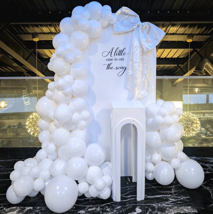 Elegant all white baby shower setup with arched backdrop and balloon styling at Nova Park Royal in London