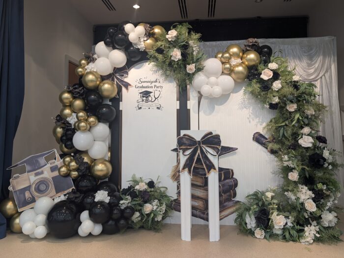 Custom graduation party decor for Sumaiyah with personalised panel, balloon arch in black, white and gold, and greenery accents